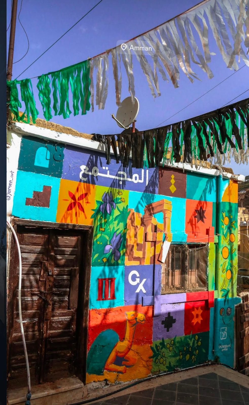 A colorful mural covering the front of a small building in Amman, with Arabic lettering, geometric patterns, and figures celebrating Jordanian culture