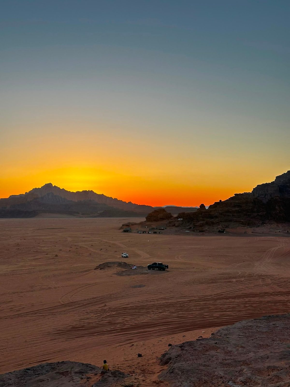 Sunset over the desert of Wadi Rum, Jordan, with the sky fading from orange to blue above dark mountains
