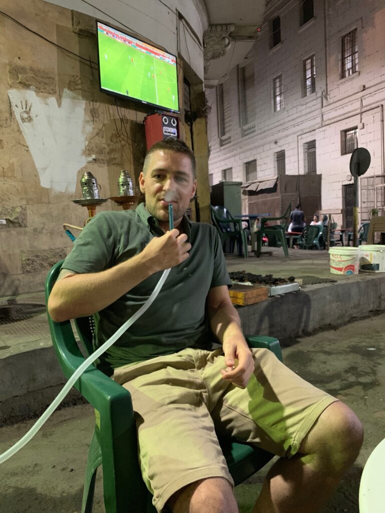 Eivind smoking shisha with a football match playing behind him