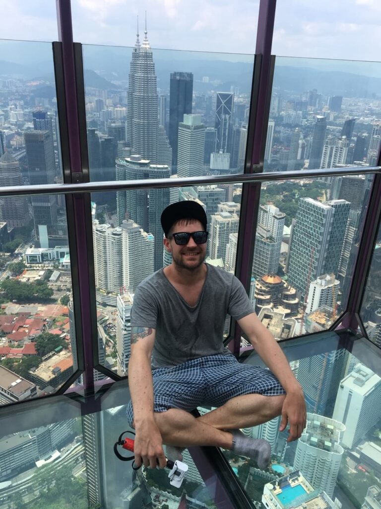 Eivind from Norway Couchsurfing posing with a casual yoga posa above a transparent flooring in a tower in Malaysia